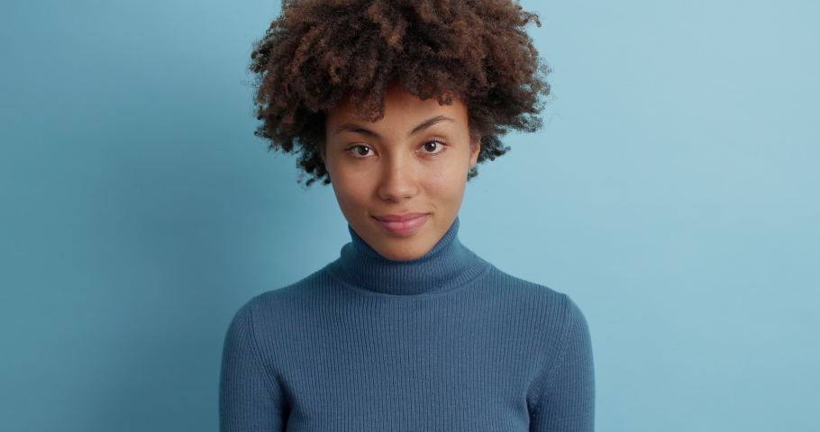 Shh be quiet please. Mysterious dark skinned Afro American woman presses index finger to lips makes silence gesture tells secret winks eye and wears casual poloneck poses against blue background Royalty-Free Stock Footage #1062743320