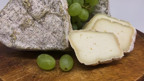 A plate of assorted mouldy goat's milk cheeses on a wooden Board with green grapes
