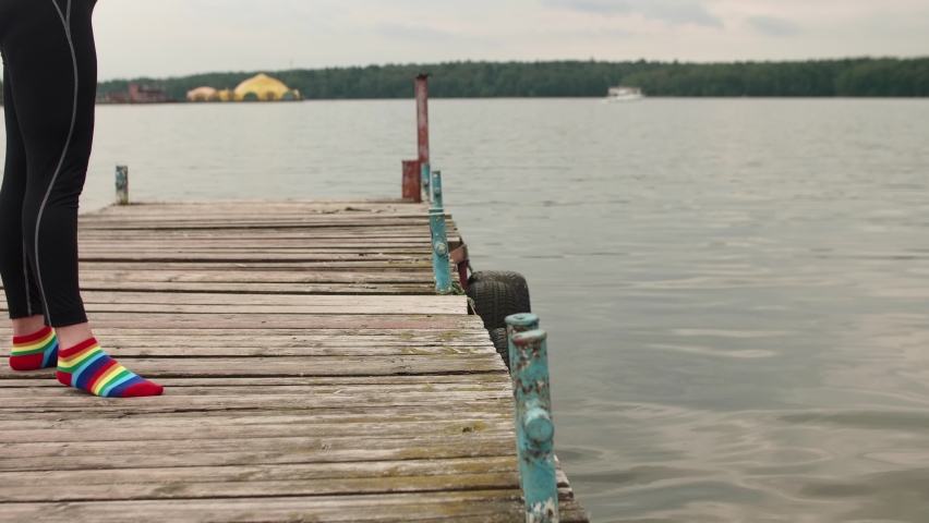 Woman lies down on old pier on pond and washes her hands on water. Sports in summer.