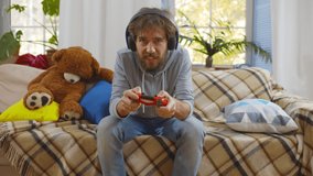 Man in headphones using joystick and playing video game while little son glued to floor with duct tape. Exhausted parent taped kid to floor and relaxing on couch with console