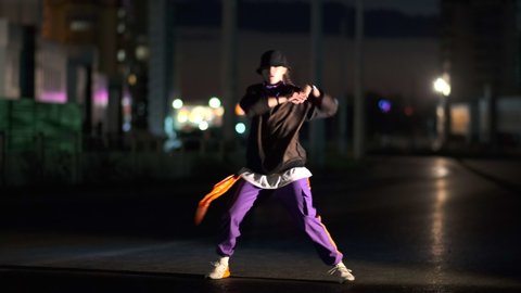 Cheerful young woman dancing hip hop, freestyle at night on a city street.