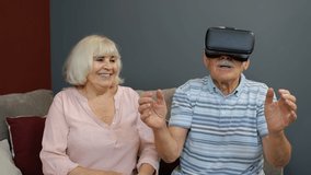 Enthusiastic grandfather and grandmother with VR headset helmet play games, watch virtual reality 3D 360 video. Family of senior man and woman at home. Future technology. VR goggles, glasses