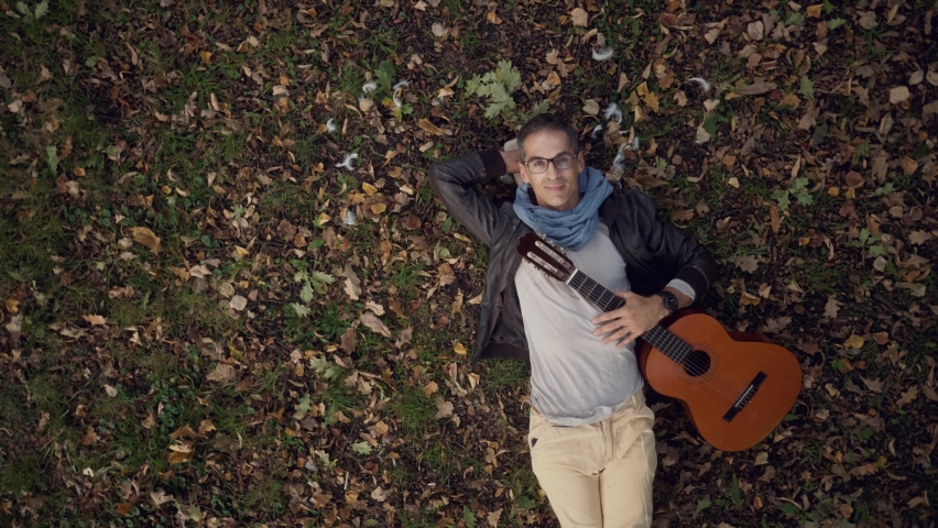 Handsome guitarist lying under the tree