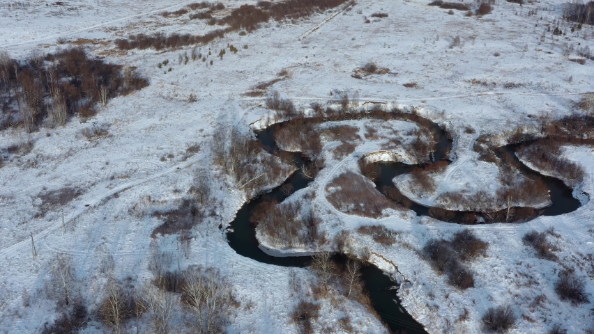 Aerial video of Koen river under ice and snow. Beautiful winter landscape. Cameramoves backwards. Novosibirsk, Siberia, Russia