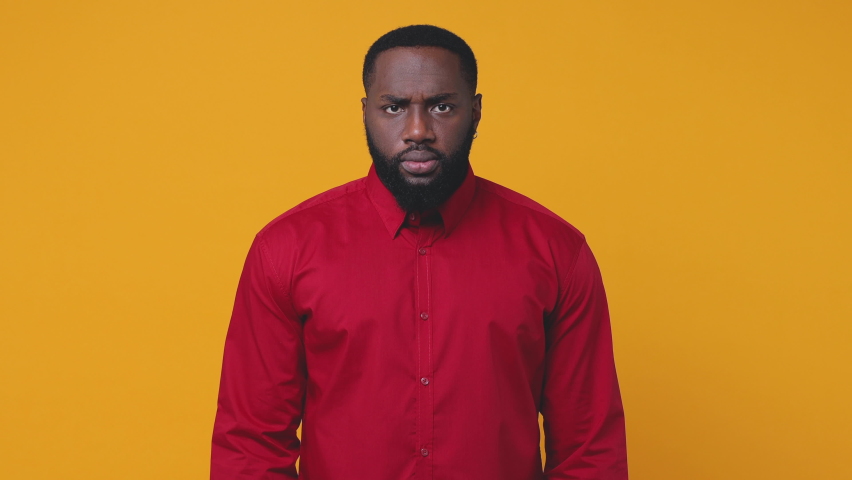 Displeased dissatisfied young bearded african american man 20s in red shirt posing isolated on yellow background studio. People lifestyle concept. Looking camera spreading hands screaming swearing | Shutterstock HD Video #1062752956