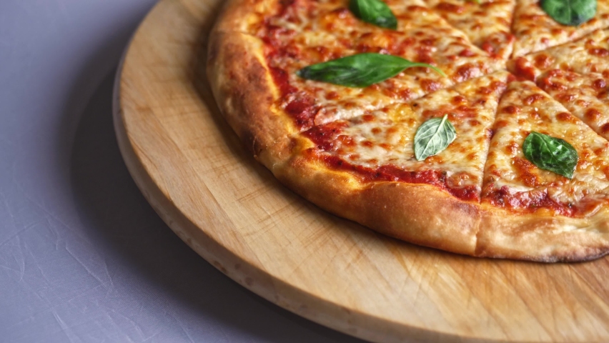 Cheese pizza with basil leaves rotating continually on a wooden plate on white table detail