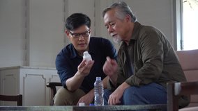 asian young son checking label on medication and giving the medicines pills to senior father. old dad suffering from illness has a young caregiver man  to take care at home - Powered by Shutterstock - Get 15% off with code: PIKWIZARD15
