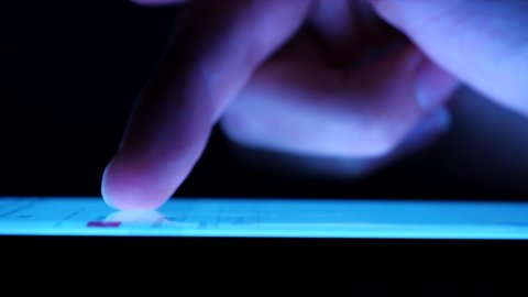 Man browsing the internet on his smartphone in a dark room. Finger hovering over a bright mobile phone screen, tapping it Side view, macro, extreme closeup Surfing the web on mobile device in darkness