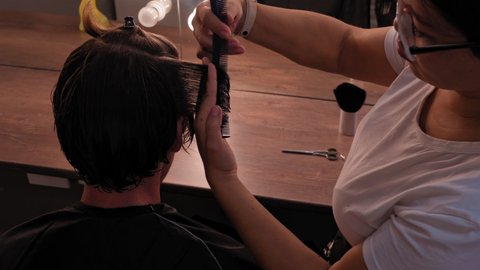 View from above. The hairdresser woman trims the temporal part of the young man and pulling her hair cuts off the ends. High definition footage. 