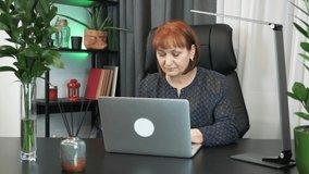 Businesswoman is finishing to work on laptop computer at office in the evening. Attractive middle-aged caucasian woman is working on laptop, typing on keyboard and looking at screen. Corporate concept