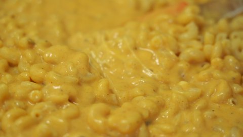 POV closeup video shows a silicone spatula stirring the most creamy, rich and delicious macaroni and cheese.