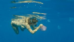 Woman in mask and fins swims and collects plastic debris under surface of blue water. Snorkeler cleaning Ocean from plastic pollution. 4K-50fps. (Complete video consists of two parts, the PART #2.). 
