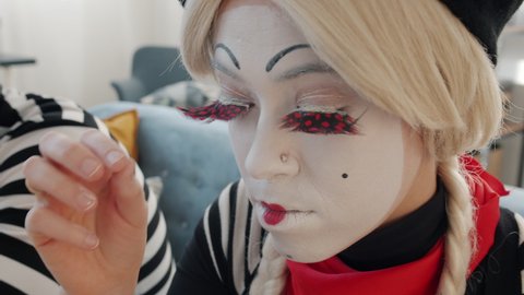 Young woman mime artist is removing make-up and face paint after performance using tissue. Backstage actress activities and cosmetics concept.