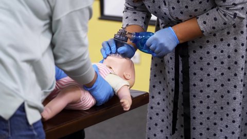 Medical mannequin doll for emergency aid. Training for giving first aid to a toddler. Breathing apparatus in woman's hands on a dummy of a child.