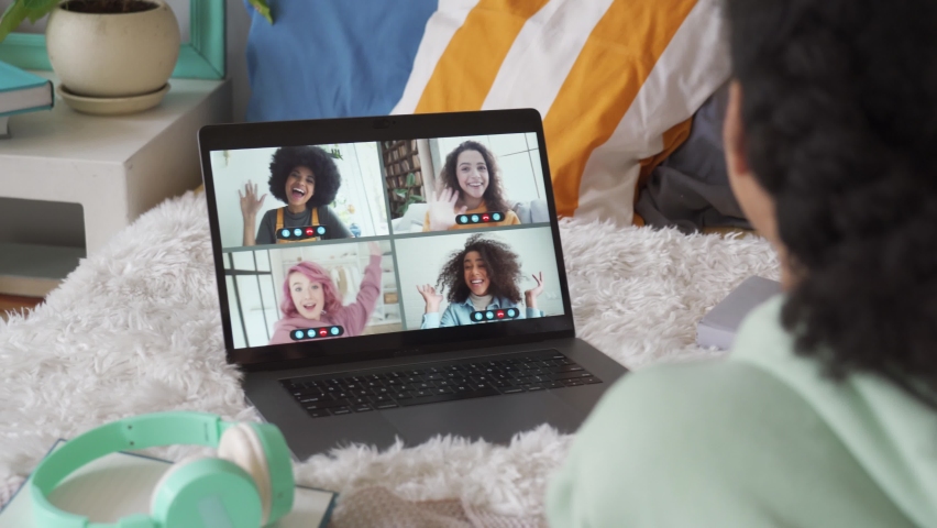 African teen girl talking to happy multicultural diverse teenage friends in online virtual chat group video call conference distance meeting using laptop computer lying on bed, over shoulder view. | Shutterstock HD Video #1062772363