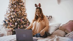 Social distancing and new normal. Young plus size woman talking with family via video call on laptop, sitting at home near Christmas tree