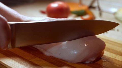close-up of cook chef hands woman cuts raw meat chicken breast on a wooden board.