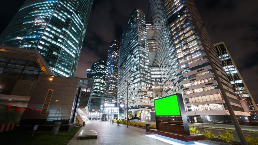 Modern billboard with a green screen on a busy street of the big city in the night. Road traffic and gigantic skyscrapers glittering with neon lights and pedestrians passing by in motion timelapse. Royalty-Free Stock Footage #1062778360
