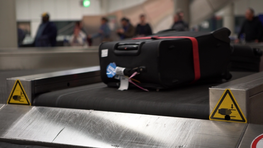 4k, Suitcase on luggage conveyor belt in the baggage claim at arrivals lounge of airport international terminal building. People picking up suitcases and bags in the waiting area. Journey concept-Dan
