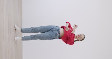 vertical video of mixed race girl recording dance moves at camera in front of white wall background. Social media concept