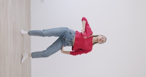 vertical video of attractive girl recording dance moves at camera in front of white wall background. Social media concept
