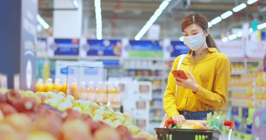 asian young businesswoman wearing face mask is shopping for fresh organic fruits and check shopping list with smart phone at supermarket during virus epidemic outbreak Royalty-Free Stock Footage #1062781207