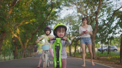 Sport activity for children. Asian young kids playing small bicycle and scooter riding on road outdoor in the park. The little girls exercise for healthy and wellbeing. Child development concept.