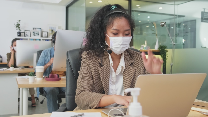 Asian young business man and colleague working on computer in office with new normal lifestyle. Group of call center people wear protective face mask and keep distancing to prevent covid virus. Royalty-Free Stock Footage #1062785293