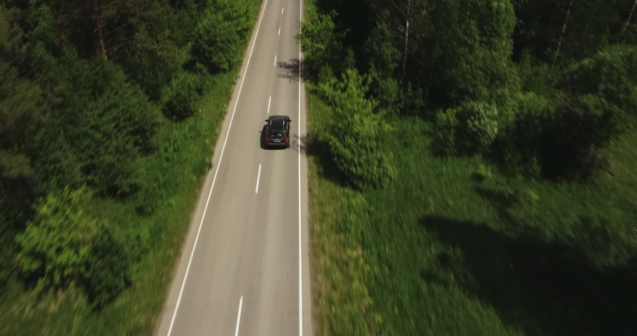 One black SUV car driving alone, travel on empty straight asphalt road freeway through dense forest corridor at summer sunny day. Aerial drone wide view. Royalty-Free Stock Footage #1062785806