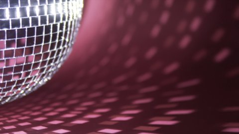 A mirror ball (disco ball) rotates on a red background. Abstract reflections of light on the background from a mirror ball. Different camera angles, speed of rotation.