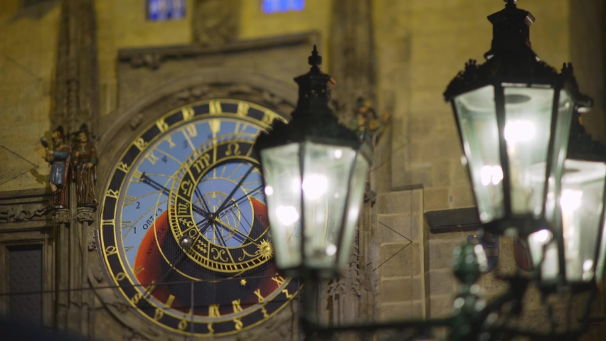 Close-up bright illuminated streetlight lantern against dial on picturesque astronomical clock tower downtown Square of Prague under heavy rain at dark night