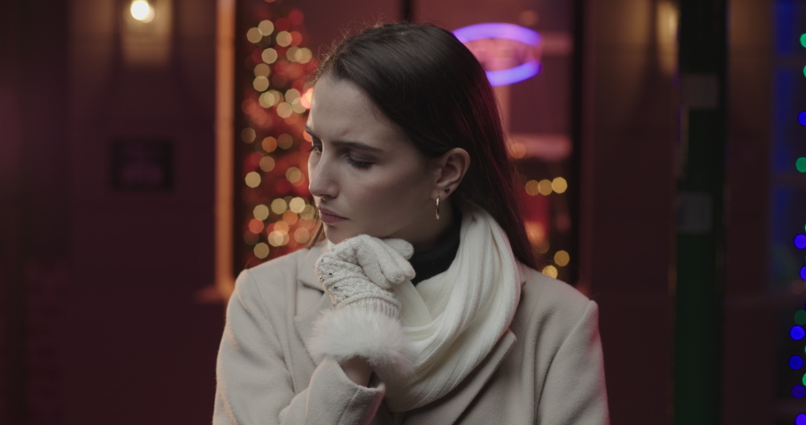 A young beautiful woman is looking thoughtful with a hand on her chin. She wears a white coat and she