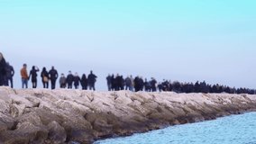 People walk along long rocky pier near tranquil azure ocean