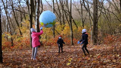 Two girls and a small boy in medical masks play in the autumn Park with a large inflatable ball. The concept of protection FROM covid-19 coronavirus infections. Slow motion 120 fps