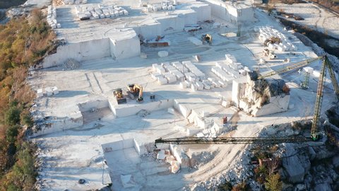 White marble quarry - construction rocks mining in an open-pit mine. Cut stone blocks and heavy machinery. Aerial drone footage.