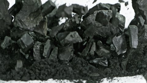 Super Slow Motion Shot of Coal Falling into Black Powder on White Background at 1000 fps.