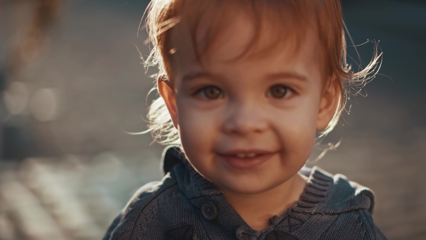 Outdoor close up portrait of little adorable child looking at the camera and smiles. Kid, parenting, happy and joyful emotions, carefree, funny face, discover new world. Concept of a happy childhood. | Shutterstock HD Video #1062802120