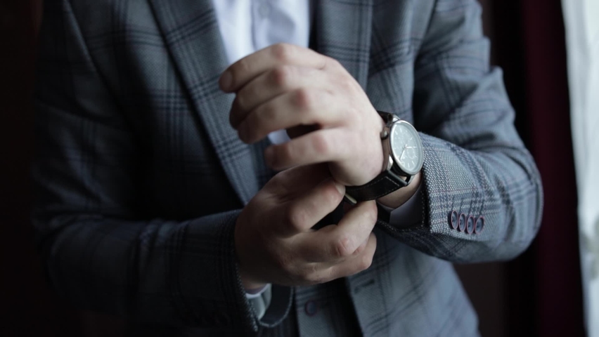 Young man in suit put on wrist watch. Groom dresses. Handsome male businessman is waiting for a meeting. Hand with a clock close up. Waits. Looks at the clock, time. Wristwatch on man arm. Slow motion Royalty-Free Stock Footage #1062803401