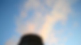 Blurred background. Black silhouette of a pipe with smoke on a background of clear sky bottom view