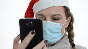 A young girl in a medical mask, in a New Year's Santa Claus hat, talks on video communication with her friend