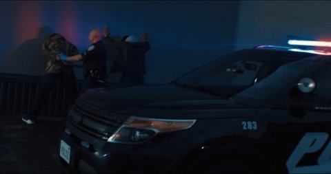 WIDE Police officer searches two suspects in the street at night. Police car lights flashing in the background. Shot with RED cinema camera and 2x Anamorphic lens