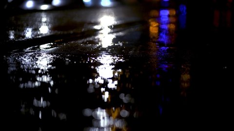 Blue lights of emergency vehicle reflecting from wet ground during rainstorm in Munich. Illuminated city during dark rainy night