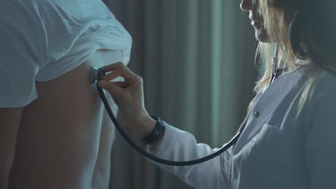 female doctor listening to her patient's back with a stethoscope.
Female doctor using her stethoscope to listening her male patient's lung while he breath.