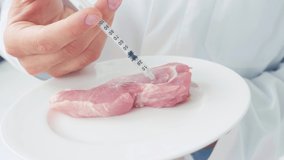 Cropped view of scientist injecting syringe in raw piece of pork on plate