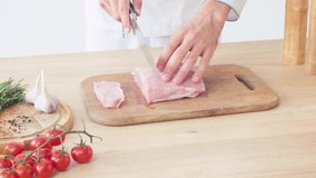 Cropped view of chef slicing pork tenderloin on chopping board on white