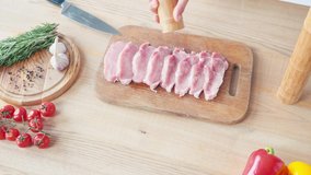 Cropped view of chef with mill seasoning slices of pork on chopping board