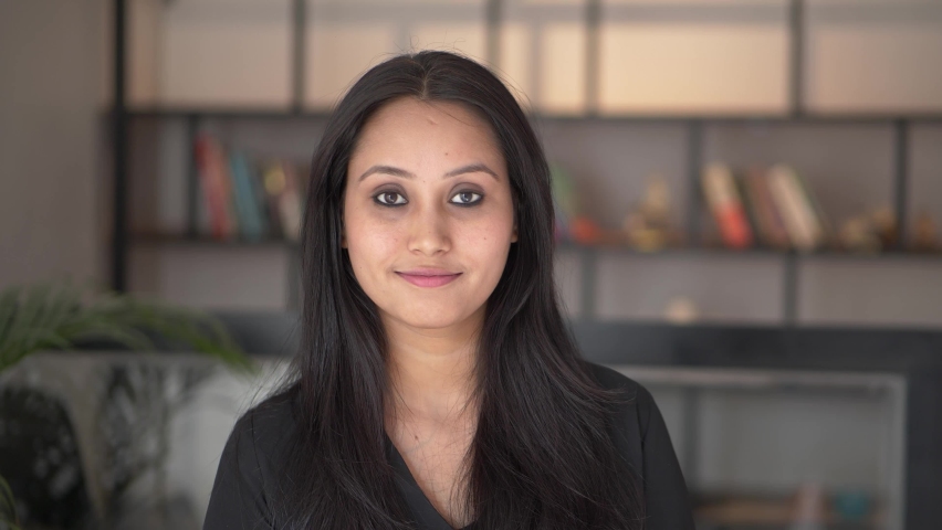 Beautiful smiling confident young Indian ethnic woman pretty face looking at camera posing alone at home in office, happy millennial Hindu ethnicity girl student professional close up front portrait. | Shutterstock HD Video #1062819772