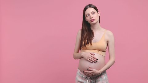Thoughtful pregnant woman future mom in basic top stroking keep hands on belly tummy with baby finger up with new idea isolated on pink background studio. Maternity family pregnancy gynecology concept