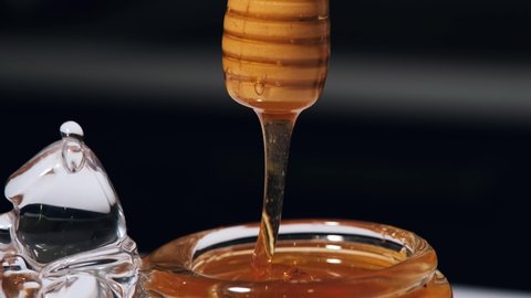 Honey dripping, pouring from honey dipper in glasses bowl. Close-up. Healthy organic Thick honey dipping from the wooden honey spoon, closeup. Healthy Food Concept. Slow motion