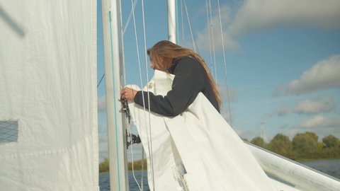 A beautiful young sportswoman studies the rigging and rigging of a sports yacht. Learning to raise a sail.